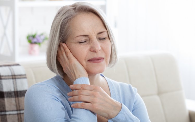 Photo of a woman covering her ear with a pain look on her face