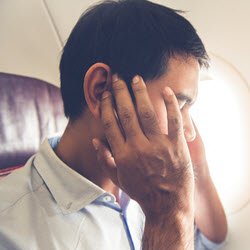 Photo of man putting his hands on his ears while seated in an airplane