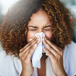 Photo of a woman sneezing into a tissue