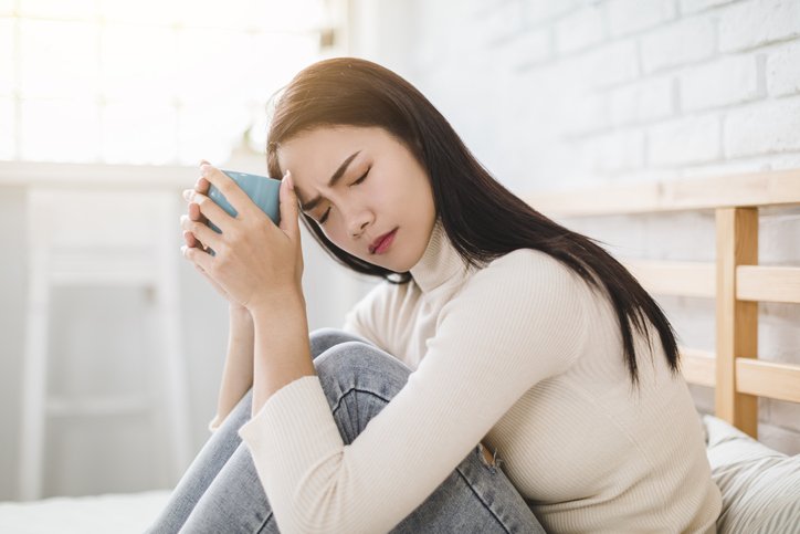 Photo of a woman frowning with her eyes closed while holding a cup of tea