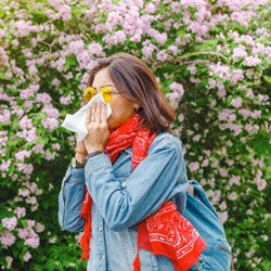 Photo of woman sneezing into a tissue outdoors