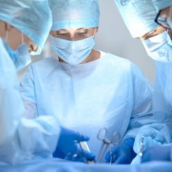 Photo of a group of surgeons in blue scrubs operating on a patient