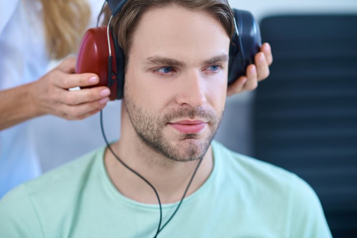 Photo of a young man with headphones being placed on his ears for a hearing test